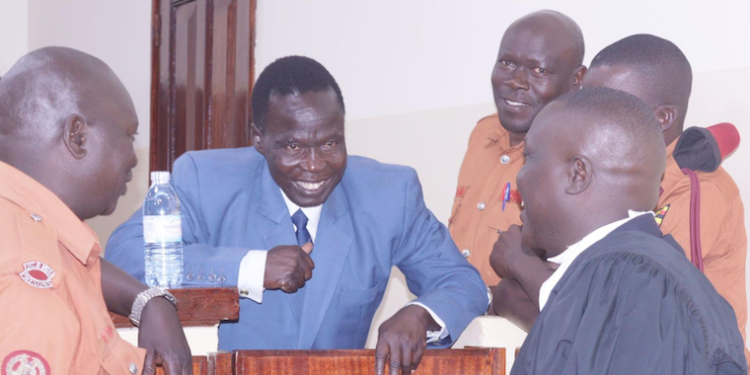 Thomas Kweyelo interacts with his lawyers and guards.